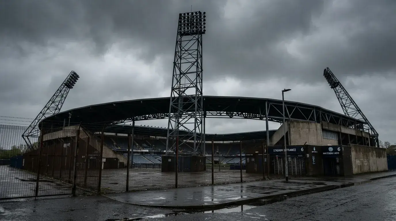Ein leeres Stadion von außen, hohe Flutlichtmasten vor einem grauen Himmel mit Regenwolken.